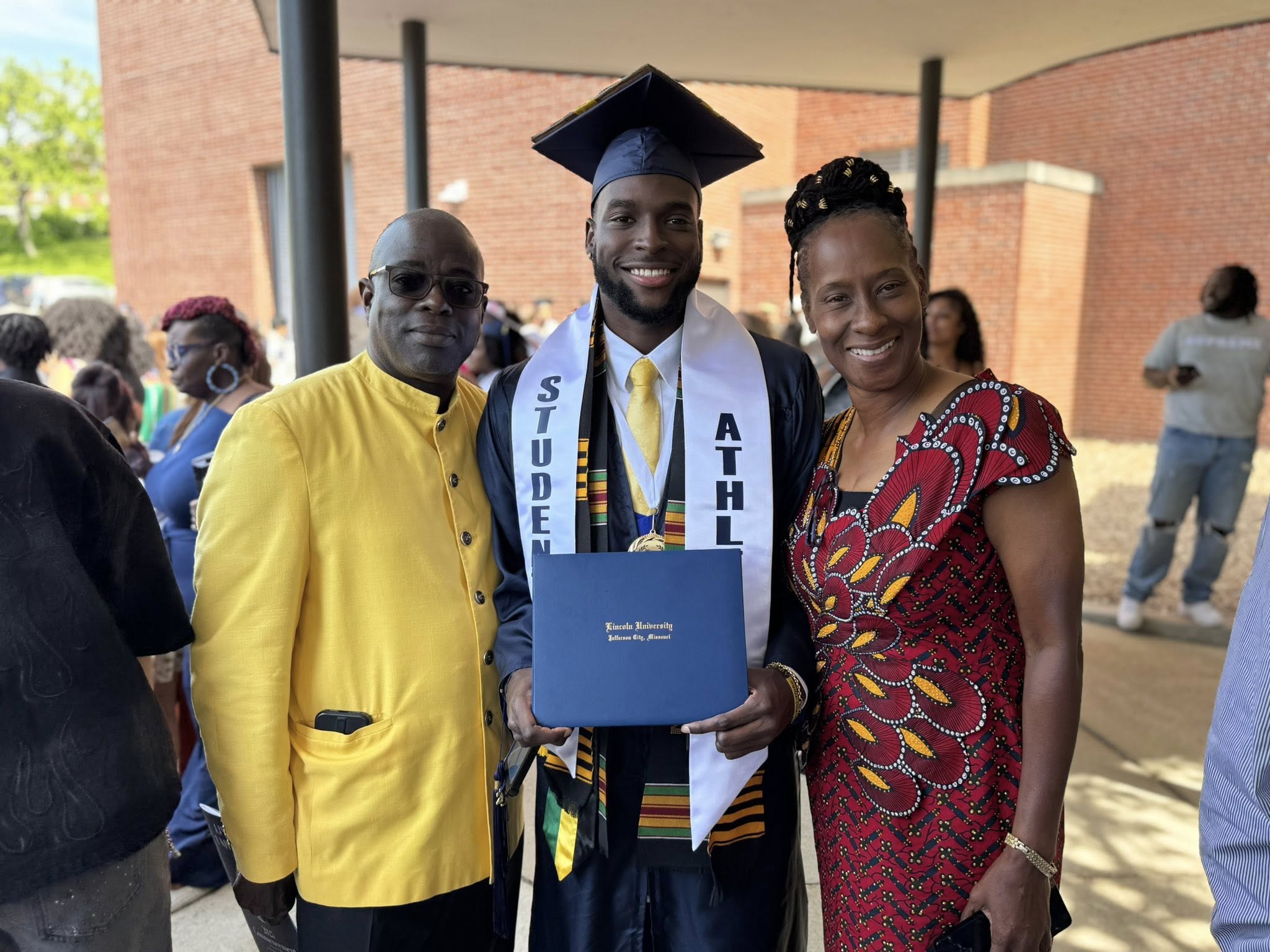 A Lincoln University of Missouri student athlete and graduate stands with his parents outside following the graduation ceremony.