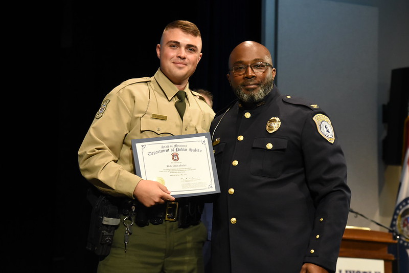 Lincoln University cadet Blake Fischer receives certificate from officer during 2025 Law Enforcement Academy award ceremony on stage.