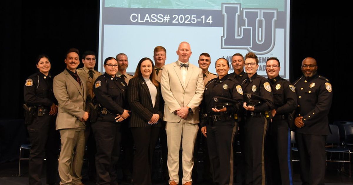 Group photo of Lincoln University Law Enforcement Academy Class #2025-14 with instructors and officers on stage at graduation ceremony.